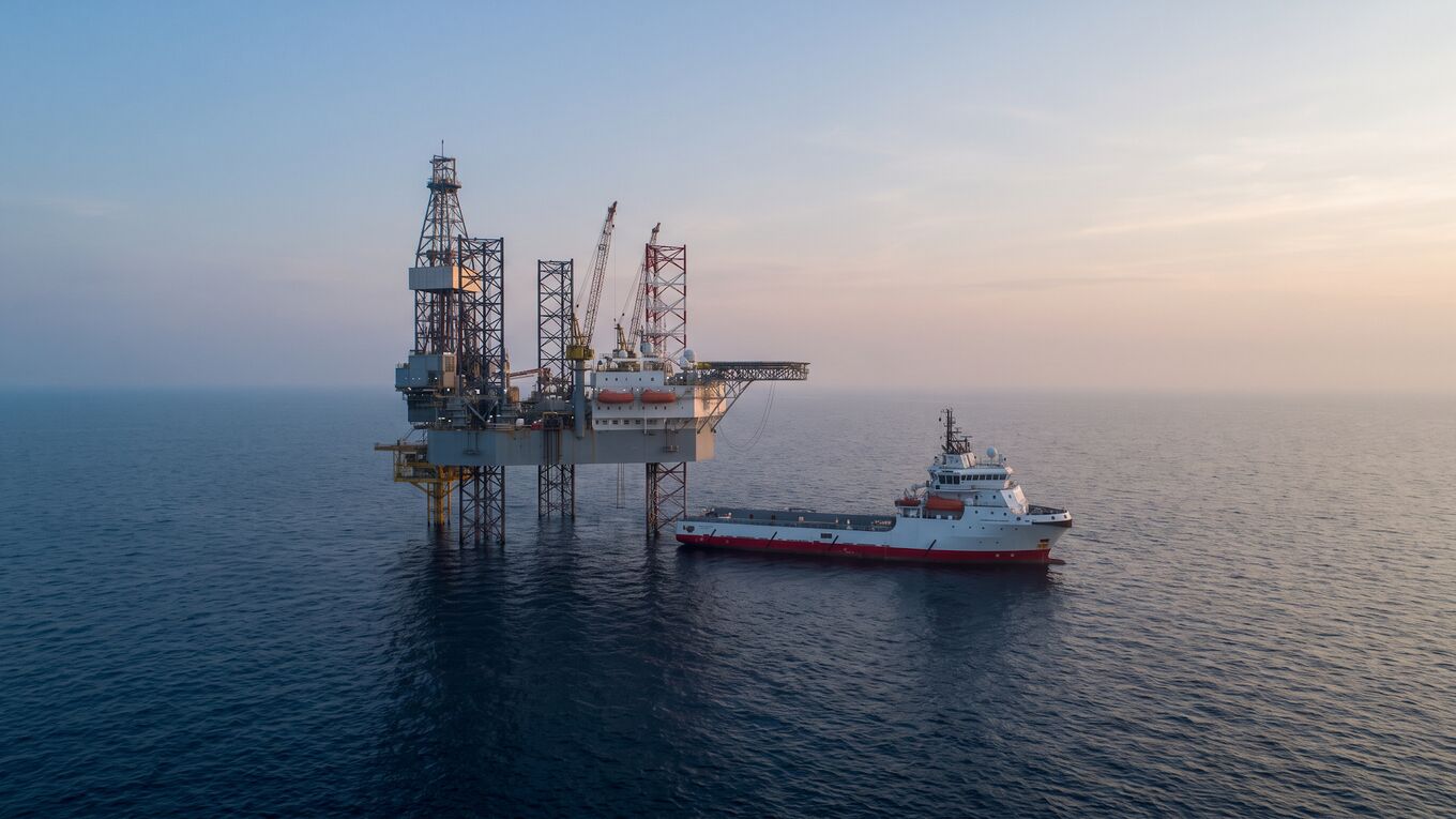 Jack-up drilling rig in the Gulf of Mexico at dawn with an offshore supply vessel alongside, seen from the water