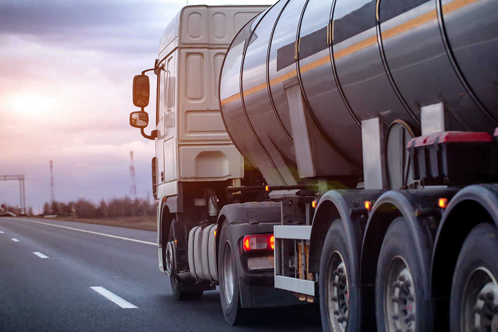 White semi-truck with dark tank trailer transporting